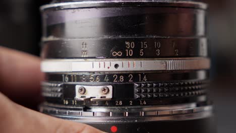 Close-up-shot-of-hands-turns-vintage-camera-lens-focus-ring,-numbers-to-infinity