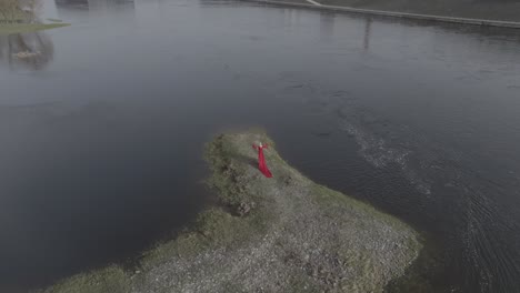 A-dramatic-drone-view-of-model-in-red-dress-walking-on-a-small-island-near-the-city