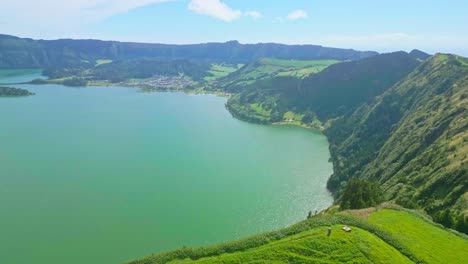 A-beautiful-green-valley-with-a-lake-and-lush-hills-under-a-bright-blue-sky,-aerial-view
