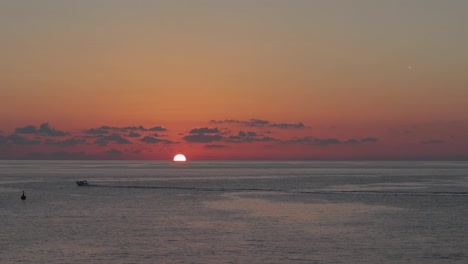 La-Colorida-Puesta-De-Sol-En-El-Mar-Mientras-El-Sol-Desaparece-Detrás-Del-Horizonte,-Con-Barcos-Deslizándose-Suavemente-Sobre-El-Agua,-Encarnando-Serenidad,-Paz,-Viajes-Y-Exploración.