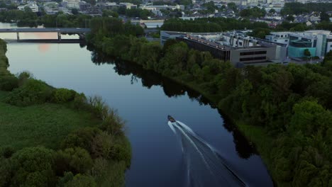 Panoramic-aerial-rearview-follows-inflatable-boat-driving-down-River-Corrib-to-Galway