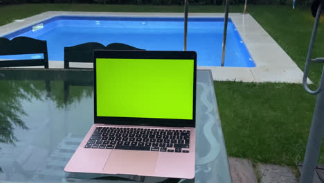 Amazing-shot-of-an-Apple-MacBook-computer-with-green-screen-on-a-table-in-front-of-a-swimming-pool-at-sunset-at-a-hotel-in-Spain