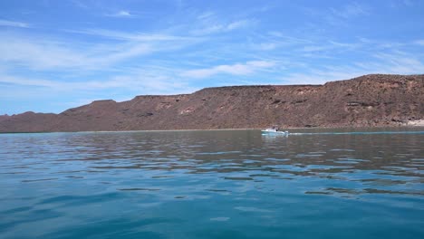 Small-boat-sailing-in-Isla-Espiritu-with-desert-landscape-in-the-background,-Santo,-Baja-California-Sur,-Mexico