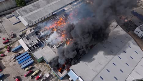 Aerial-top-down-of-black-toxic-smoke-rising-up-during-fire-in-warehouse