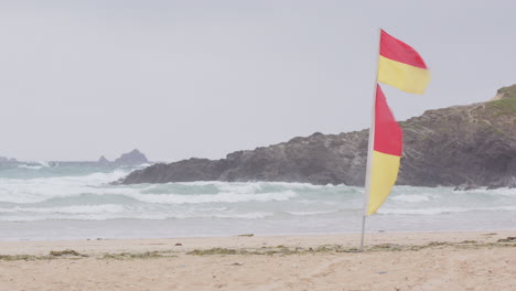 Gelbe-Und-Rote-Rettungsschwimmer-Flaggen-Flattern-Bei-Starkem-Wind-Am-Strand-Von-Cornwall