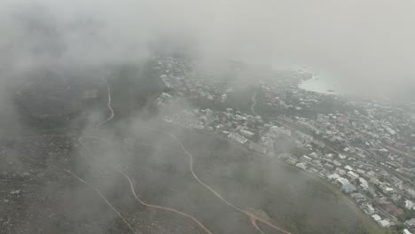 Drohne-Fliegt-Durch-Wolken-Hinunter-Zum-Camps-Bay-Beach-In-Kapstadt,-Südafrika-–-Drohne-Fliegt-Sehr-Hoch,-Und-Man-Kann-Viele-Häuser-Am-Hang-Sehen