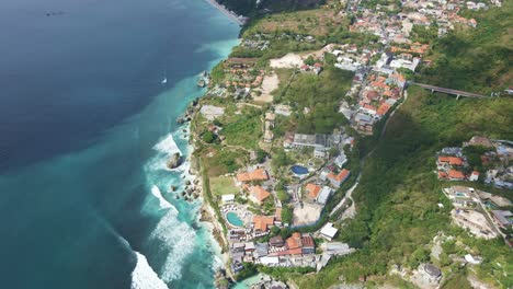 Aerial-view-of-famous-Uluwatu-Beach,-Badung,-Bali-with-beach-clubs,-resorts-and-real-estate-located-at-the-top-of-the-cliff