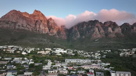 Drohne-Fliegt-Hoch-über-Camps-Bay-In-Kapstadt,-Südafrika---Viele-Häuser-Liegen-Auf-Einem-Hügel---Tafelberg-Mit-Wunderschönen-Wolken-Bei-Sonnenuntergang