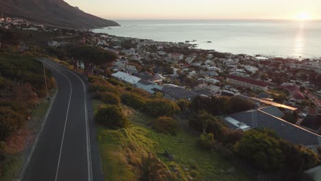 Drone-Vuela-Sobre-La-Bahía-De-Camps-En-Ciudad-Del-Cabo,-Sudáfrica---Muchas-Casas-En-Una-Ladera---Drone-Vuela-Justo-Por-Encima-De-árboles-Y-Casas-Con-Vistas-A-La-Puesta-De-Sol