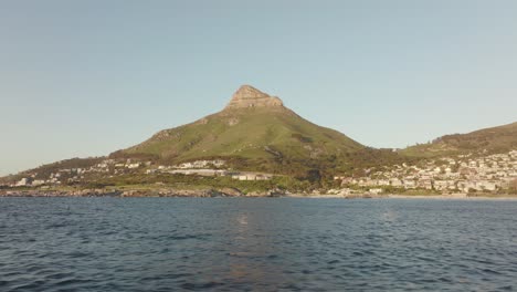 Drone-flying-sideways-over-the-sea-at-Camps-Bay-beach-in-Cape-Town-South-Africa---many-houses-on-a-hilltop---view-of-lion's-head-mountain