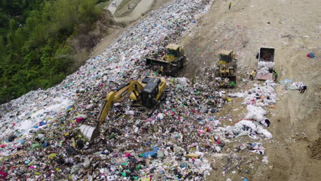 Drone-shot-of-a-landfill-with-trucks-and-tractors-managing-garbage,-highlighting-waste-disposal-and-recycling-efforts