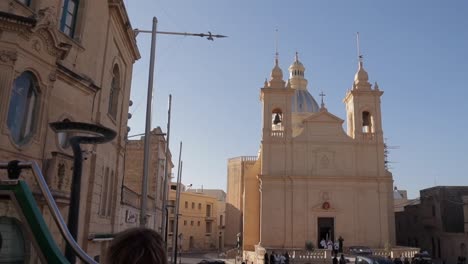 Los-Viajeros-Y-Visitantes-Se-Sientan-En-El-Piso-Superior-De-Un-Autobús-Turístico-Panorámico,-Pasando-Por-La-Iglesia-De-San-Lawrenz-En-Dwejra,-Gozo,-Malta,-Capturando-La-Esencia-De-La-Exploración-Cultural-Y-El-Turismo-Panorámico.