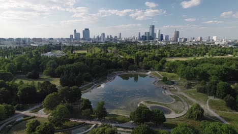 Skyline-of-Warsaw-on-beautiful-green-park-with-water-pond,-aerial-view