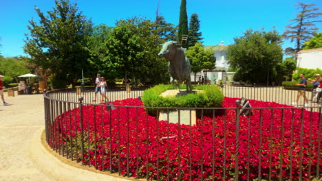 Malerische-Aussicht-Auf-Eine-Stierstatue,-Umgeben-Von-Leuchtend-Roten-Blumen-Und-Grün-In-Einem-Malerischen-Garten-An-Einem-Sonnigen-Tag