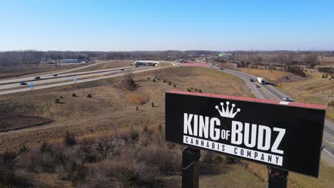 King-of-Budz-cannabis-company-logo-in-USA-near-highway,-aerial-ascend-view