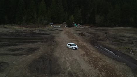 high-angle-aerial-of-a-white-car-carefully-navigating-dusty-Stave-Lake-mud-flats-Drone-flies-backwards-capturing-the-car's-cautious-progress-from-logging-roads-distant-trees-and-campgrounds