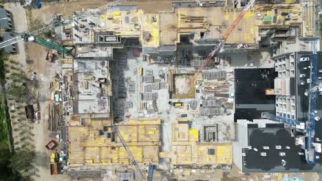 Aerial-top-down-view-on-the-rooftop-of-an-apartment-building-under-construction-with-tower-crane-and-a-lot-of-workers-laying-metal-rebar