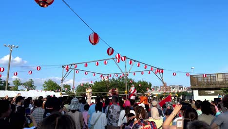 Traditional-Japanese-festival-with-a-lively-crowd,-red-lanterns,-and-taiko-drummers-under-a-clear-sky