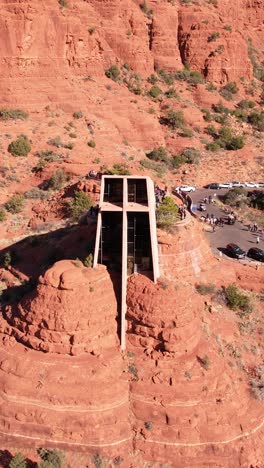 Sedona,-Arizona-USA,-Vertical-Drone-Shot,-Chapel-of-Holy-Cross-and-Visitors-Under-Red-Rock-Cliffs