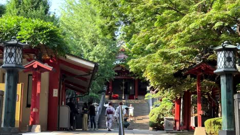 Menschen,-Die-An-Einem-Sonnigen-Tag-In-Einer-üppigen-Gartenanlage-Auf-Einen-Traditionellen-Japanischen-Tempel-Zugehen