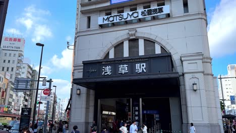 Entrance-of-Asakusa-Station-in-Tokyo-with-people-passing-by-under-a-bright-blue-sky