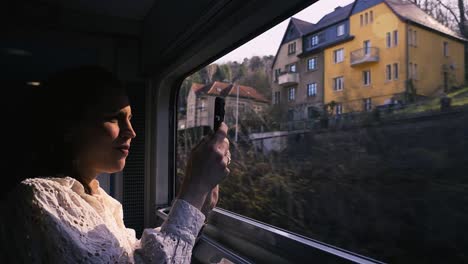 Train-passing-elbe-valley-houses-while-white-woman-makes-pictures-out-of-train-with-mobile-phone,-Bad-Schandau,-Decin,-Dresden