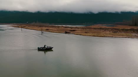 Maniobras-De-Pescador-Barco-Acercándose-A-Grant-Narrows-Parque-Pitt-Addington-Marsh-Vida-Silvestre-órbitas-Aéreas-Capturando-Agua-Tranquila-Rodeada-De-Montañas-Nubes-Suaves-Atmósfera-Cambiante-Belleza-Natural