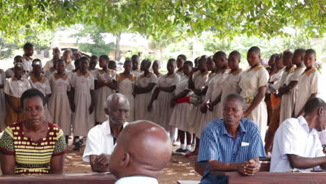 Ugandan-Students-In-Uniforms-Standing-Around-Teachers-Sitting-Outdoor-At-School-Campus-In-Kampala,-Uganda