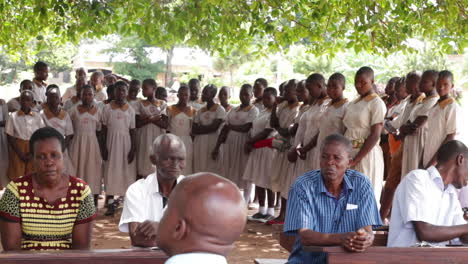 Ugandische-Schüler-In-Uniformen-Stehen-Um-Lehrer-Herum,-Die-Draußen-Auf-Dem-Schulgelände-In-Kampala,-Uganda-Sitzen