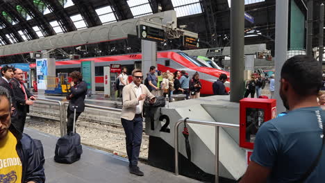 Viajeros-Ocupados-En-La-Estación-Central-De-Milán-Con-El-Tren-De-Alta-Velocidad-Rojo-En-Segundo-Plano.