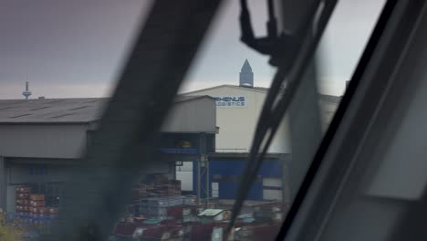 Vista-Desde-La-Ventana-De-Un-Tren-Que-Captura-Edificios-Industriales-Y-Torres-Distantes,-El-Movimiento-Borroso-Mejora-La-Sensación-De-Velocidad.