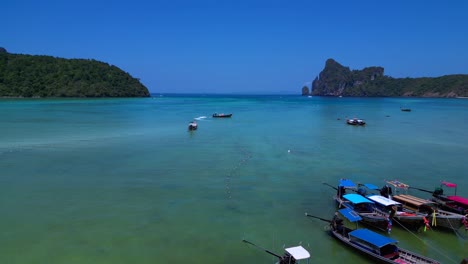 Koh-Phi-Phi-Bay,-colorful-traditional-longtail-boats-are-floating-on-calm-turquoise-water