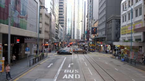 Busy-street-in-Hong-Kong-from-tram-POV-with-shops,-people,-and-tall-buildings-in-view