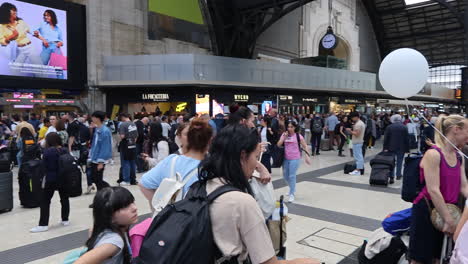 Busy-travelers-at-Milan-Central-Station-with-luggage,-waiting-under-arrival-and-departure-boards