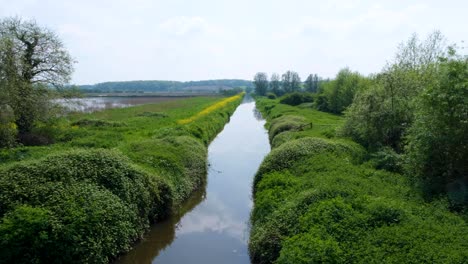 Long-straight-drainage-stream-river-of-water-between-agricultural-farmland-fields-on-the-Somerset-Levels-in-England-UK