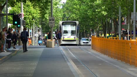 Trams-depart-from-the-stop-on-Swanston-street-in-front-of-State-Library-Victoria,-with-commuters-waiting-at-the-stop-in-the-bustling-Melbourne-central-business-district,-a-vibrant-urban-lifestyle