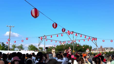 Outdoor-festival-with-traditional-Japanese-performers-and-colorful-lanterns-under-a-clear-blue-sky