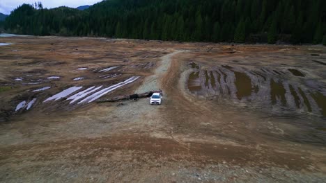 Drone-flying-fast-in-reverse,-camera-tracking-a-white-Toyota-parked-on-a-muddy-flat