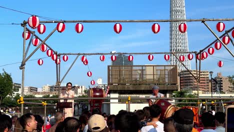 Outdoor-festival-with-traditional-drumming-and-lanterns,-large-crowd,-blue-sky,-Tokyo-Tower-in-background