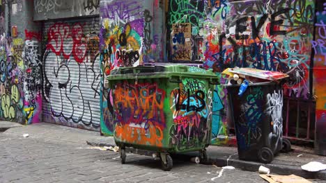 People-visiting-Hosier-Lane,-a-popular-cobblestone-laneway-featuring-a-vibrant-array-of-art-murals-and-graffiti-on-the-exterior-walls-of-buildings-with-overflowing-rubbish-from-the-wheelie-bins