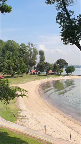 Portraitaufnahmen-Von-Sonnigem-Meerblick-Mit-Kleinen-Pavillons,-Bänken,-Bäumen-Und-Sandstrand-Auf-Einer-Tropischen-Insel