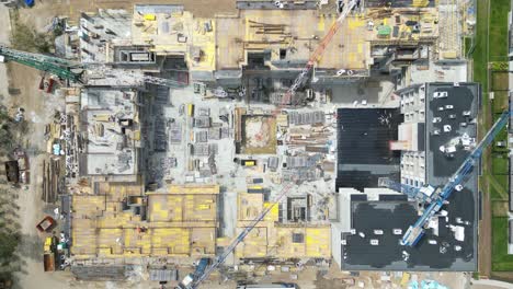 Aerial-top-down-view-on-the-rooftop-of-an-apartment-building-under-construction-with-tower-crane-and-a-lot-of-workers-laying-metal-rebar