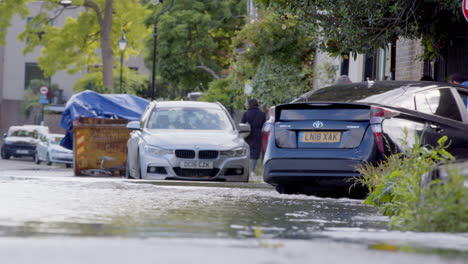 Car-drives-through-flooded-London-street-with-pedestrian-activity,-low-angle