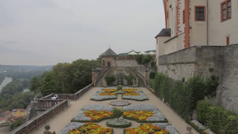 View-from-Bamberg-Castle-garden-overlooking-river,-vibrant-flowers-line-the-path,-architectural-beauty