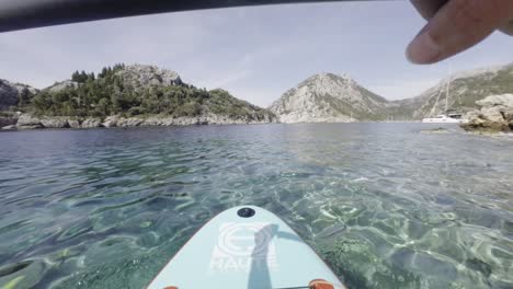 A-close-up-of-a-person-paddleboarding-in-clear-waters-near-a-rocky-coastline-in-Turkey,-filmed-in-2024