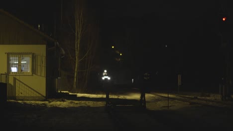 Nighttime-scene-of-a-train-approaching-a-rural-station,-illuminated-by-its-headlight-against-a-snowy-backdrop,-atmospheric-and-moody