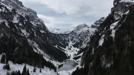 Frozen-Talalpsee-Lake-nestled-in-a-valley-with-snow-covered-trees-and-peaks,-Talalpsee,-Switzerland