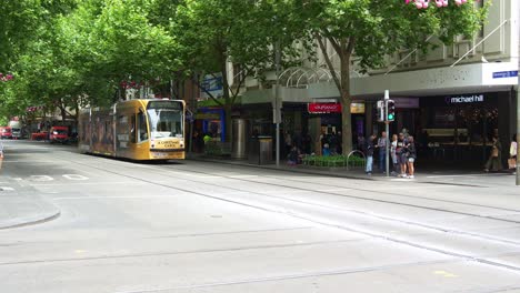 Trams-glide-along-the-tree-lined-Swanston-Street,-in-Melbourne's-bustling-Central-Business-District,-showcasing-the-vibrant-hustle-and-bustle-of-Australian-urban-life