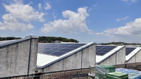 Vista-Del-Techo-De-Una-Fábrica-Llena-De-Paneles-Solares-Para-Tener-Una-Fuente-De-Energía-Sostenible-En-Un-Día-Soleado-Con-Nubes-En-El-Fondo