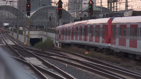 Deutsche-Bahn-train-approaching-a-station-with-modern-cityscape-in-the-background,-evening-light